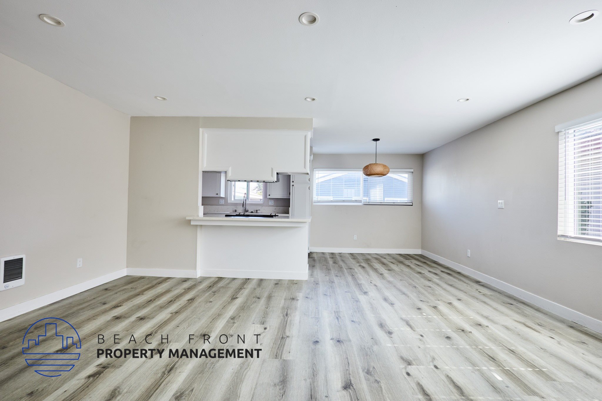 A spacious room with wooden flooring and a logo for Beach Front Property Management in the corner.